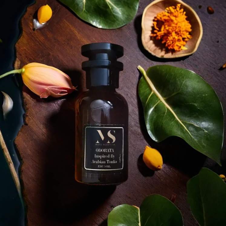 A bottle of inspired by arabians tonka unisex amber-woody perfume with top notes of Saffron and Bergamot, middle notes of Agarwood and Bulgarian Rose, and base notes of Sugar Cane, Tonka Bean, Amber, White Musk, and Oakmoss, presented on a dark background with leaves and a flower around it.