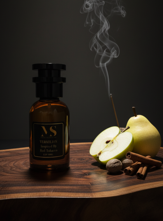 A bottle of inspired by red tobacco perfume with a lit incense stick, half-cut apple, pear, and cinnamon sticks on a wooden surface.